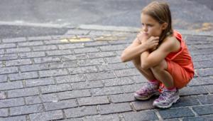 Niña de cuclillas sola en la calle